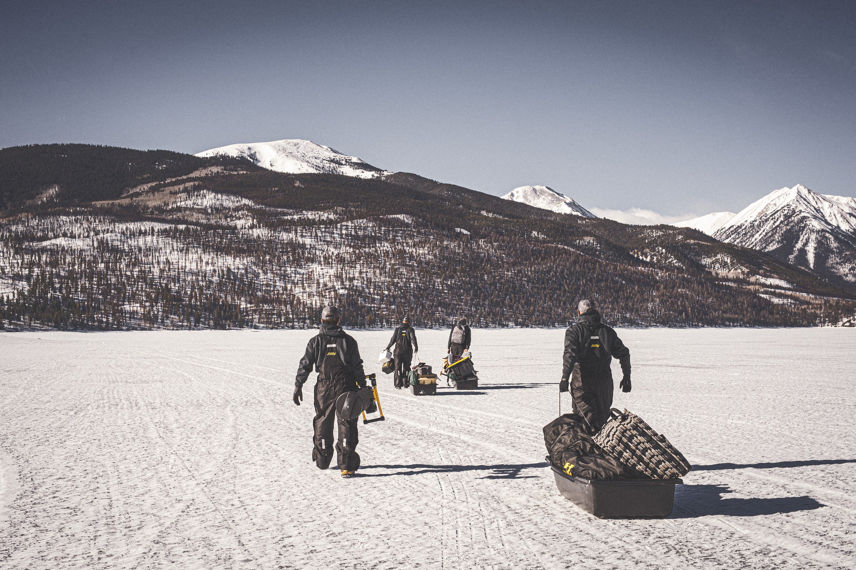 People with fishing gear on a frozen lake with snow-covered mountains in the background